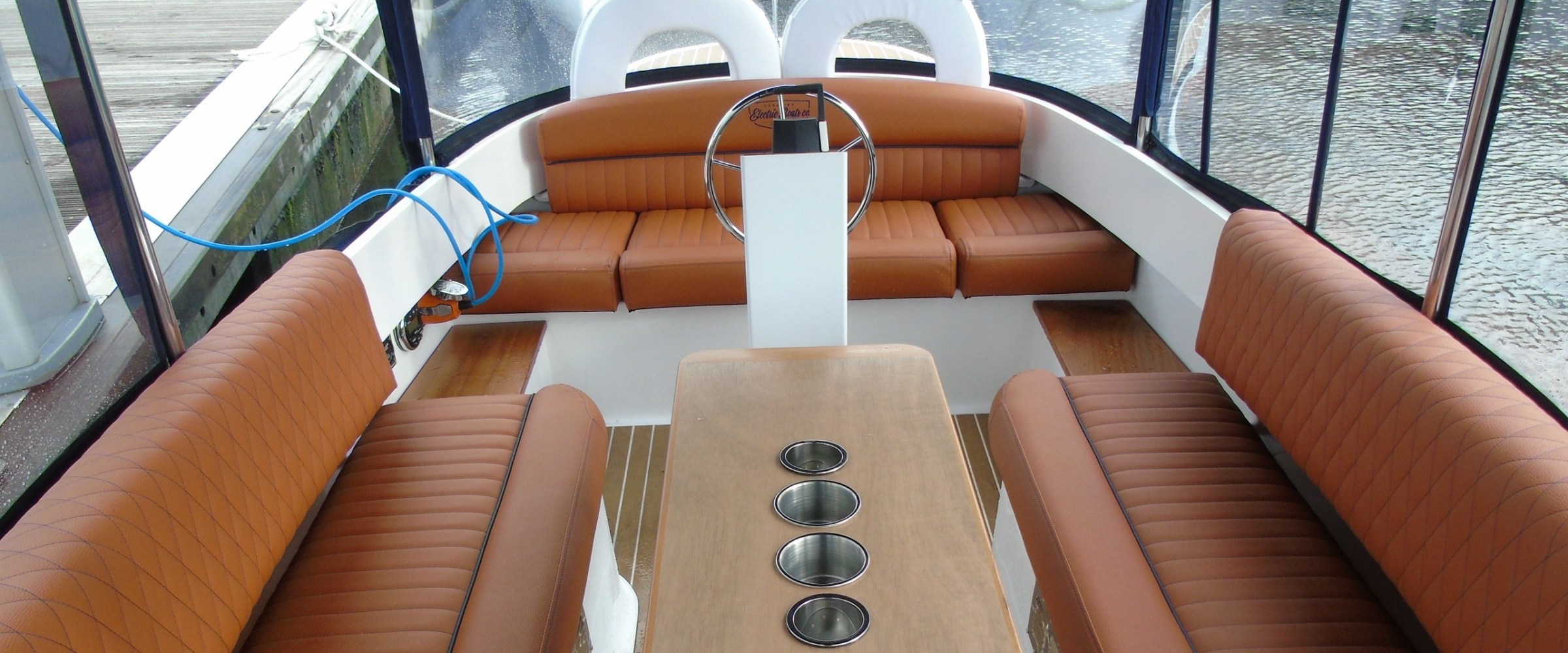 Interior of a boat with brown leather seats and a wooden table with cup holders.