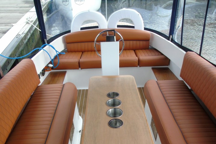 Interior of a boat with brown leather seats and a wooden table with cup holders.