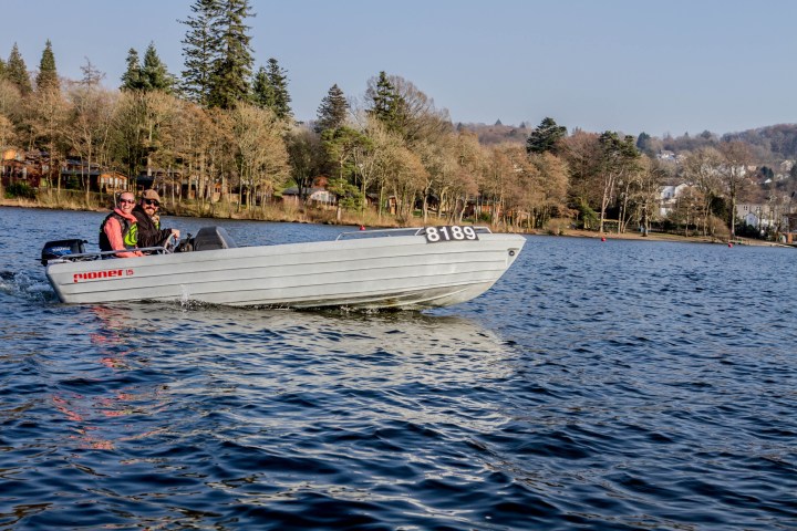 Two people in a small motorboat on a lake, surrounded by trees.