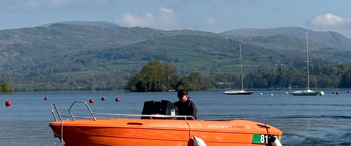 Orange motorboat on a lake with distant hills and a clear blue sky.
