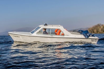 White cabin cruiser boat with orange life rings on a lake under clear blue sky.