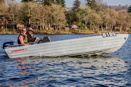 Two people in a motorboat cruising on a lake near a wooded shore.