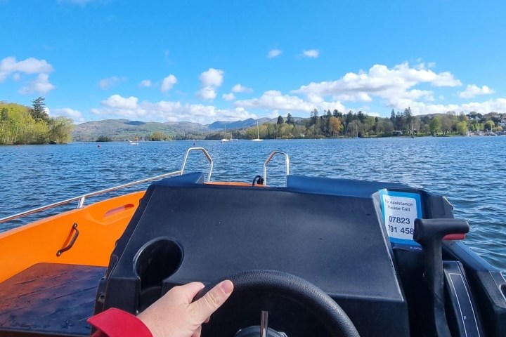 View from a small boat on a lake, with mountains and trees in the background.