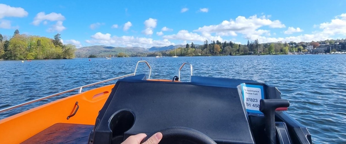 View from a small boat on a lake, with mountains and trees in the background.