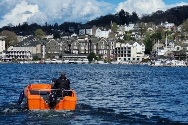 Person in orange boat on lake with town and hills in background.