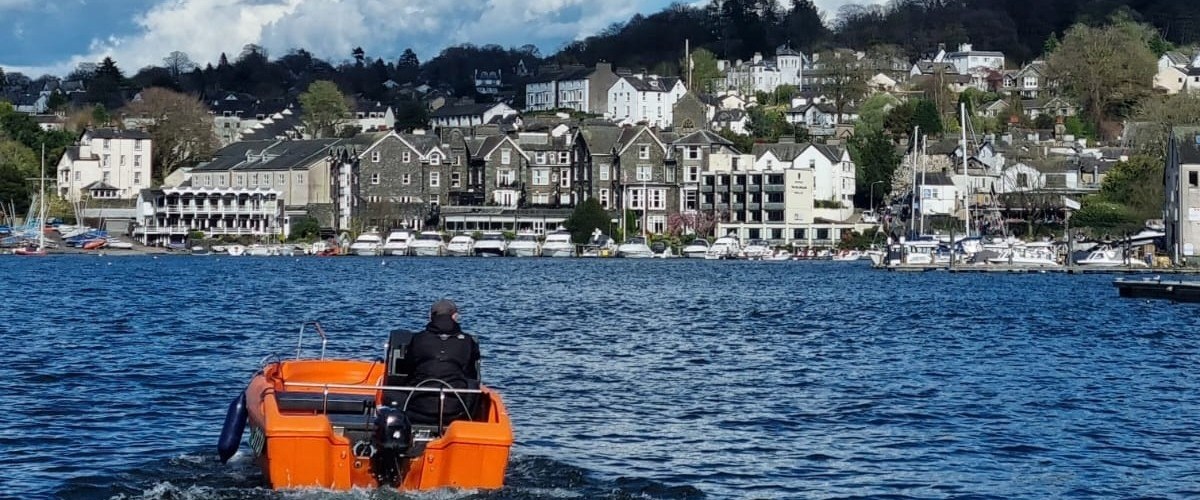 Person in orange boat on lake with town and hills in background.