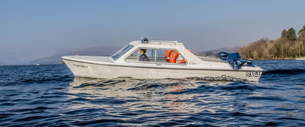White motorboat on a lake with trees and hills in the background.