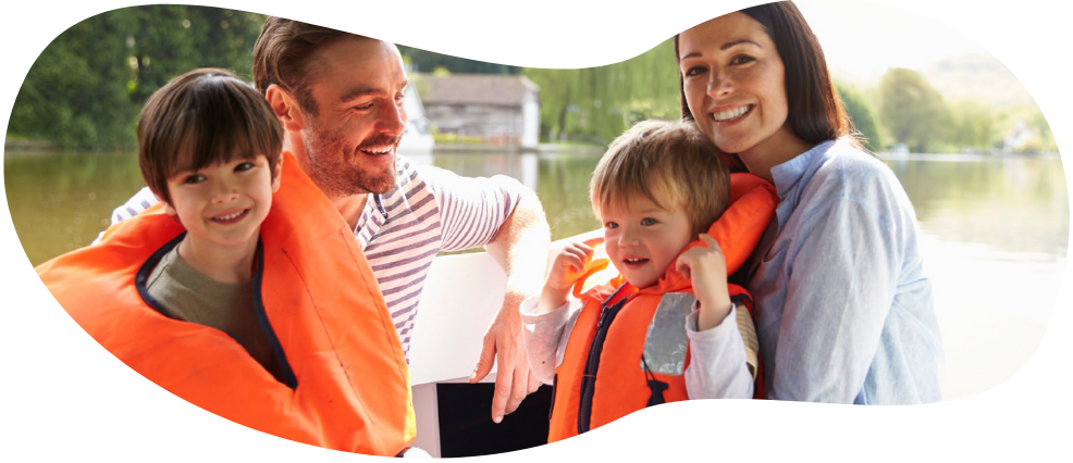 Family of four wearing orange life jackets near a lake.