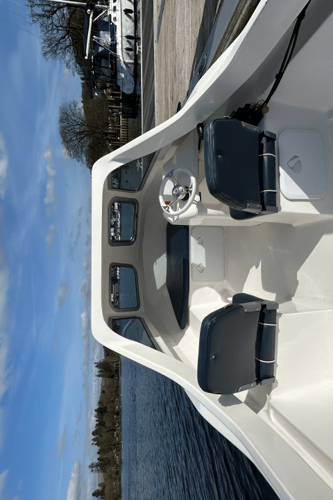 View of a boat interior with two seats and a steering wheel under a clear sky.