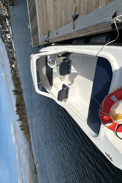 Small white boat with a lifebuoy moored at a dock on a sunny day.
